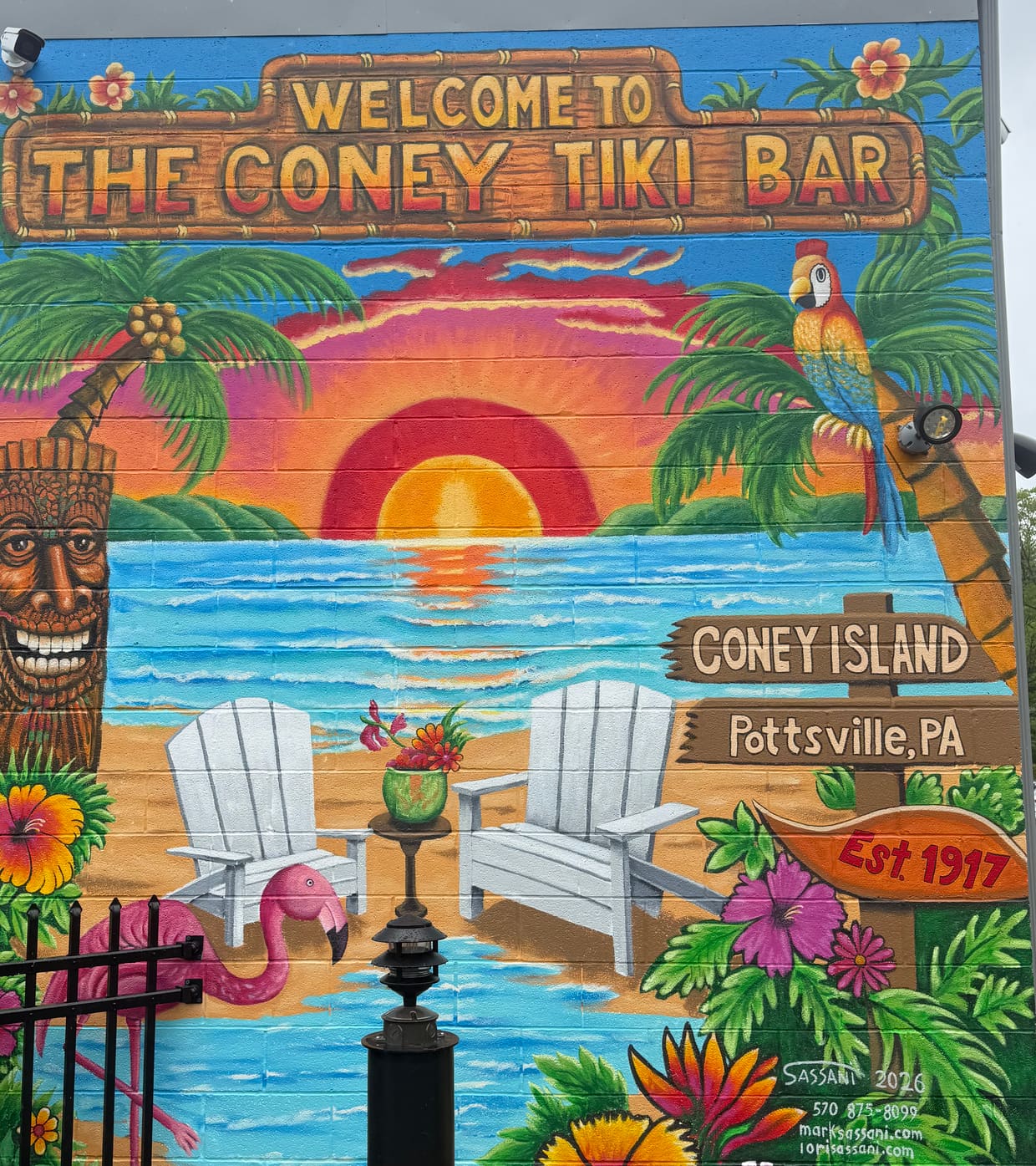 Hand-painted Coney Tiki Bar mural at The Coney Island in Pottsville, Pennsylvania, showing a tropical sunset, Adirondack chairs, a pink flamingo, a parrot, palm trees, and the Coney Island Pottsville Est. 1917 sign.