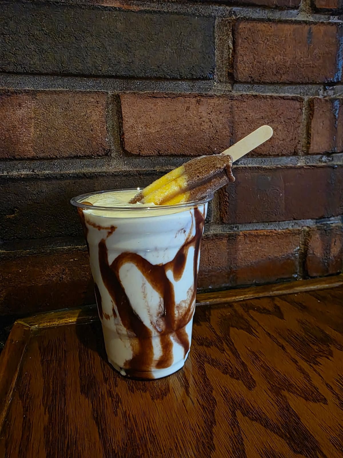 A Premium Deluxe Milkshake with chocolate drizzle and a two-tone ice-pop garnish, in front of the brick wall at The Coney Island in Pottsville, PA.